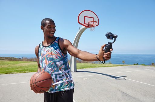 Social influencer posing with a basketball for a selfie-stick camera on a beautiful sunny day. This cool basketball court overlooks the ocean.