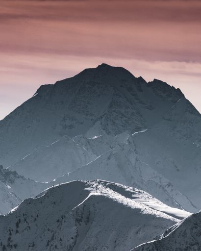 A vertical shot of the snow covered mountain peaks under the colorful cloudy sky