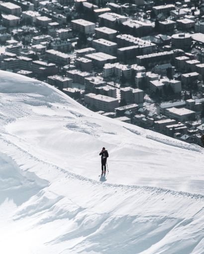 A vertical shot of a person with ski equipment standing on a snow covered cliff