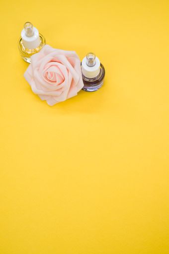 A vertical shot of essential oils next to a beautiful pink rose on a yellow surface