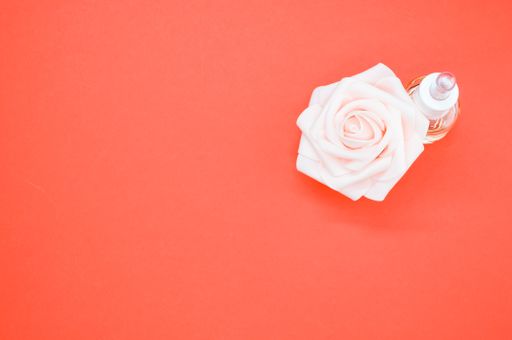 A high angle shot of essential oil next to a beautiful pink rose on a peach-colored surface
