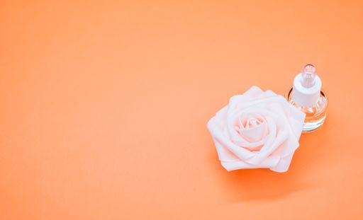 A high angle shot of essential oil next to a beautiful pink rose on an orange surface