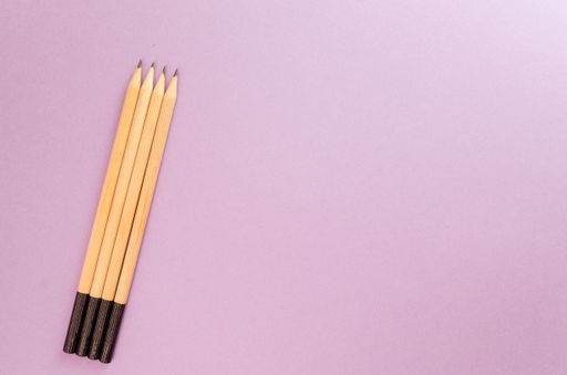 A top view of four pencils assorted on a purple surface, with space for text