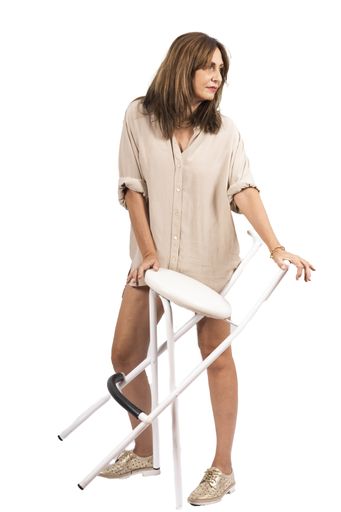A vertical shot of a beautiful middle-aged Hispanic woman wearing an oversized shirt next to a stool in front of a white background
