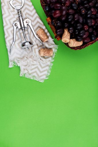 A vertical shot of fresh ripe grapes, corks, and corkscrew against green background