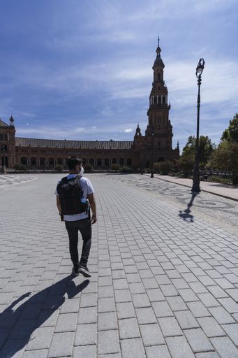 A vertical shot of a young man walking near the Plaza de Espana in Seville, Spain wearing a sanitary mask - concept of the new normal