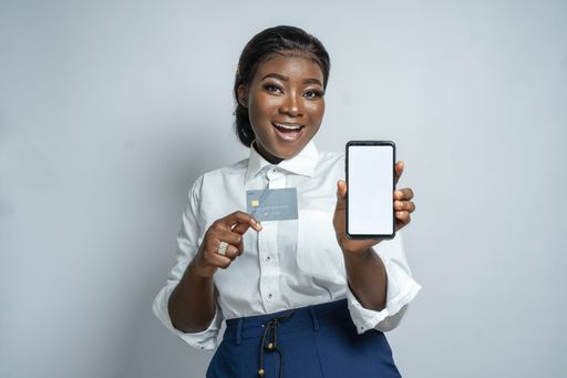 A beautiful young African woman happily recommending online shopping and easy payment while holding a card and a blank smartphone