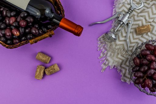 A bottle of wine, fresh ripe grapes, corks, and corkscrew on purple background