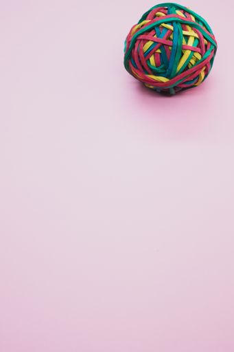 A vertical shot of a rubber ball made out of rubber bands isolated on a pink background