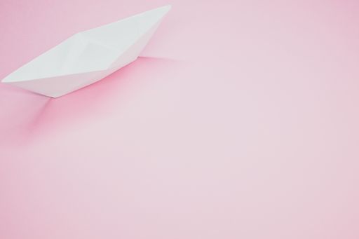 A top view of a white paper boat isolated on a pink background