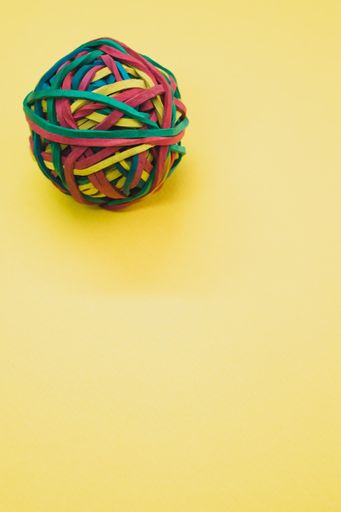 A vertical shot of a rubber ball made out of rubber bands isolated on a yellow background