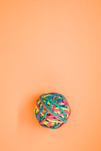 A vertical shot of a rubber ball made out of rubber bands isolated on an orange background