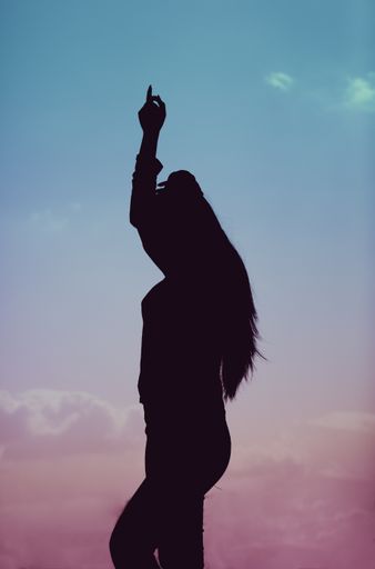A vertical shot of a silhouette of a female dancing during a beautiful sunset