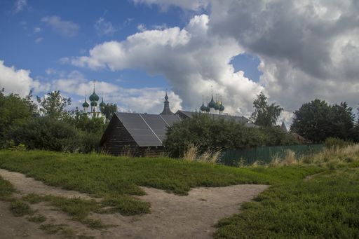 A field surrounded by wooden barns with the Rostov Kremlin under a blue cloudy sky on the background in Russia
