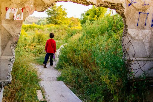 A kid walking through a pathway surrounded by a ruined building and greenery