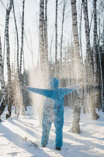 A vertical shot of a person in a fluffy blue costume standing with hands up in a forest in winter - back to childhood concept