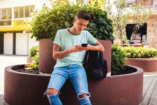 A young Hispanic man sitting while texting through his phone