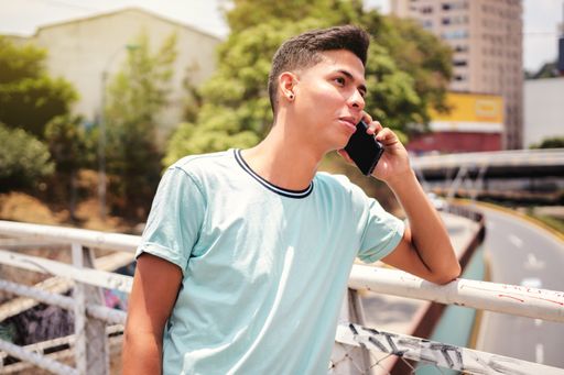 A selective focus shot of a young Hispanic man talking on cellphone on a bridge