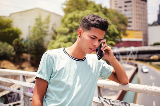 A selective focus shot of a young Hispanic man talking on cellphone on a bridge