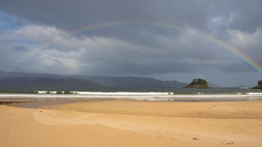 A landscape of a beach surrounded by the sea with a rainbow over it in Viveiro, Spain