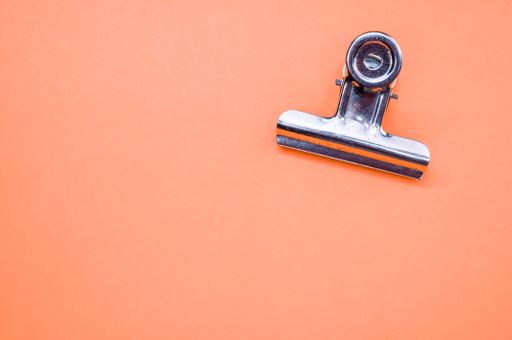 A high angle shot of a metallic paper clipper isolated on an orange background