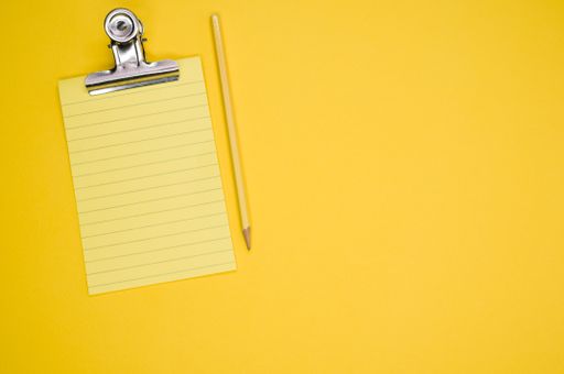 A top view of a notepad with a pencil and a paper clipper isolated on a yellow background
