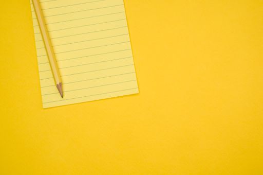 A top view of a blank notepad with a pencil isolated on a yellow background