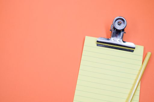 A top view of a notepad with a paper clipper and a pencil isolated on an orange background