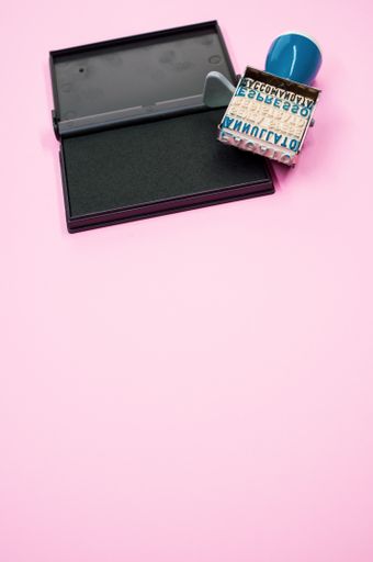 A vertical shot of a rubber stamp roller with words on it with ink isolated on a pink background