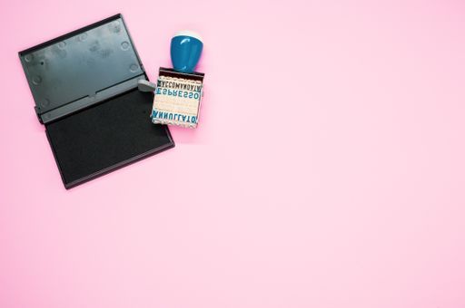 A top view of a rubber stamp roller with words on it with ink isolated on a pink background