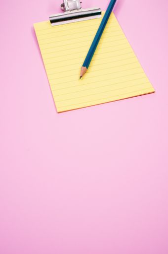 A vertical shot of a notepad with a paper clipper and a pencil isolated on a pink background