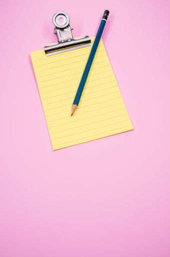 A vertical shot of a notepad with a paper clipper and a pencil isolated on a pink background