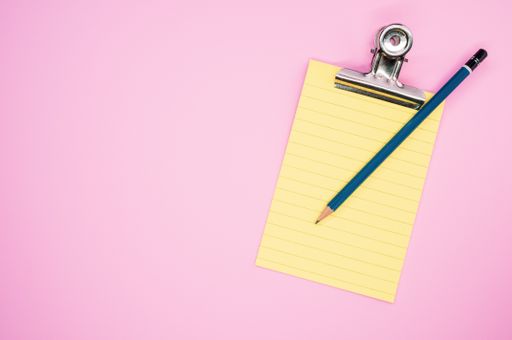 A top view of a notepad with a paper clipper and a pencil isolated on a pink background