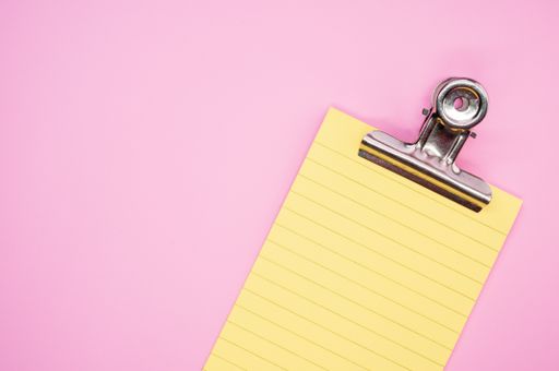 A top view of a notepad with a paper clipper isolated on a pink background