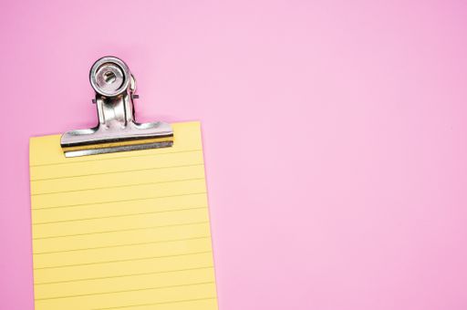 A top view of a notepad with a paper clipper isolated on a pink background