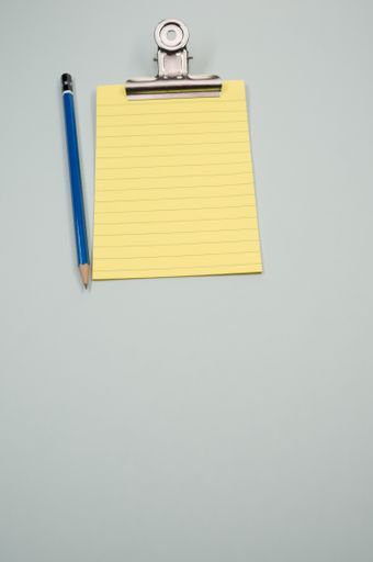 A vertical shot of a notepad with a paper clipper and a pencil isolated on a gray background
