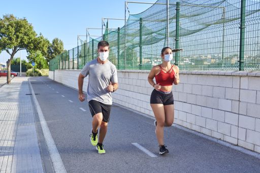A fitness instructor with a female client jogging outdoors while wearing a protective mask