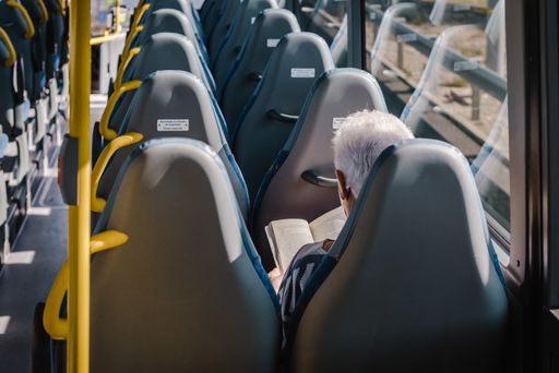 A lonely elderly person reading a book on the bus