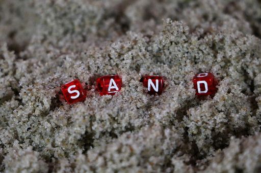 A closeup shot of letter cubes forming the word sand on the sand