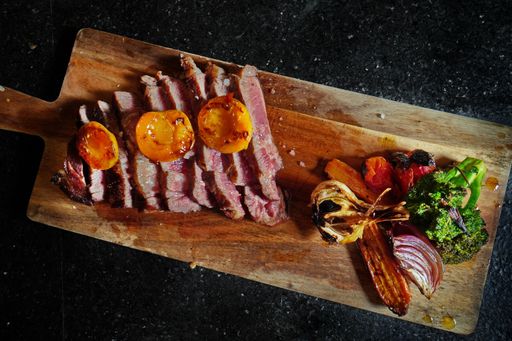 A top view of gourmet sliced red meat on a wooden cutting board with roasted vegetables