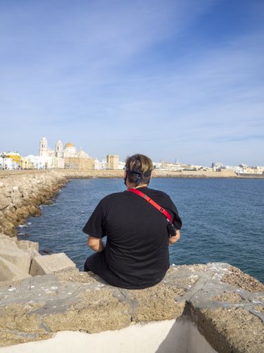 An adult male photographer sitting on the coast surrounded by the sea under the sunlight