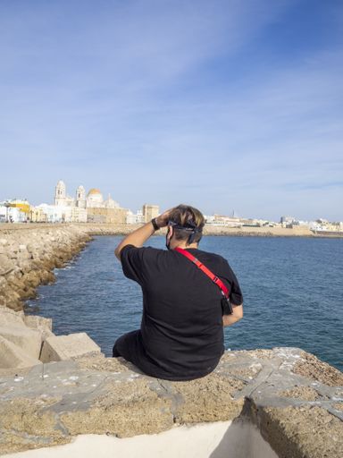 An adult male photographer sitting on the coast surrounded by the sea under the sunlight