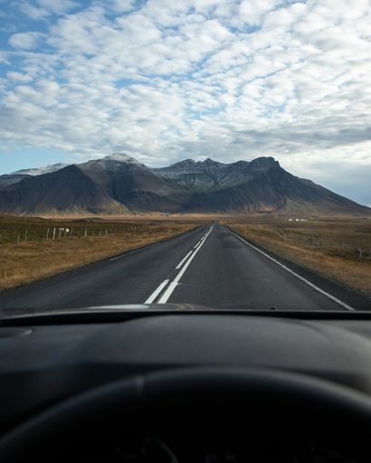 A vertical shot of a car on the road surrounded by rocky hills under a blue cloudy sky in Iceland