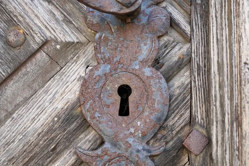 A closeup of an aged rusty and weathered metallic keyhole on a wooden door