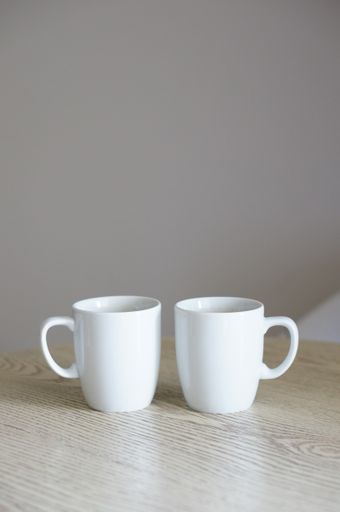 A closeup of two white cups on the table with a blurry background