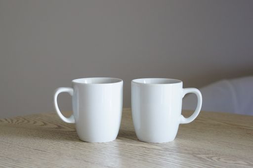 A closeup of two white cups on a wooden table with a blurry background