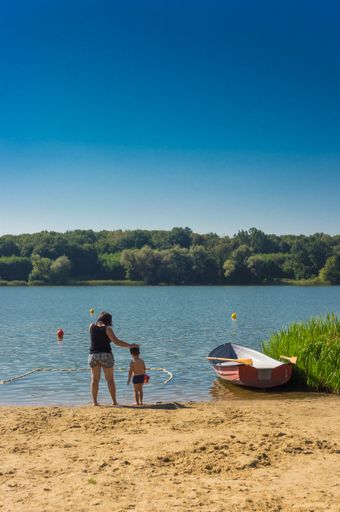 Woman and toddler boy standing in front of a lake with boat on a sunny da