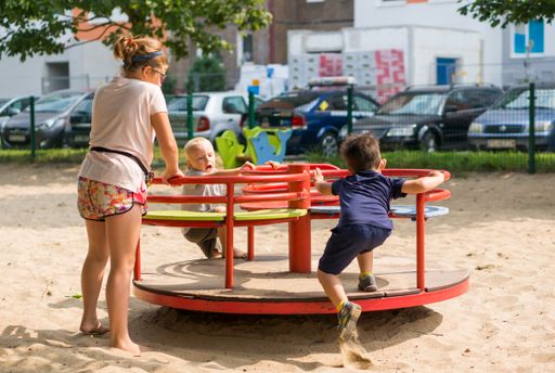 Two toddler boys and a girl playing on a roundabout at a playground on a sunny day