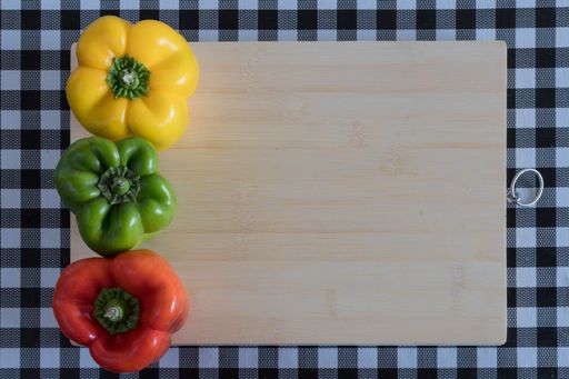 A top view of assorted peppers on a wooden board, with a black and white checkered tablecloth