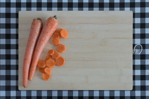 A top view of chopped carrots on a wooden board, with a black and white checkered tablecloth
